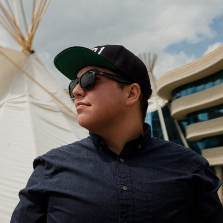 side view of a man in a hat and sunglasses standing in front of a teepee